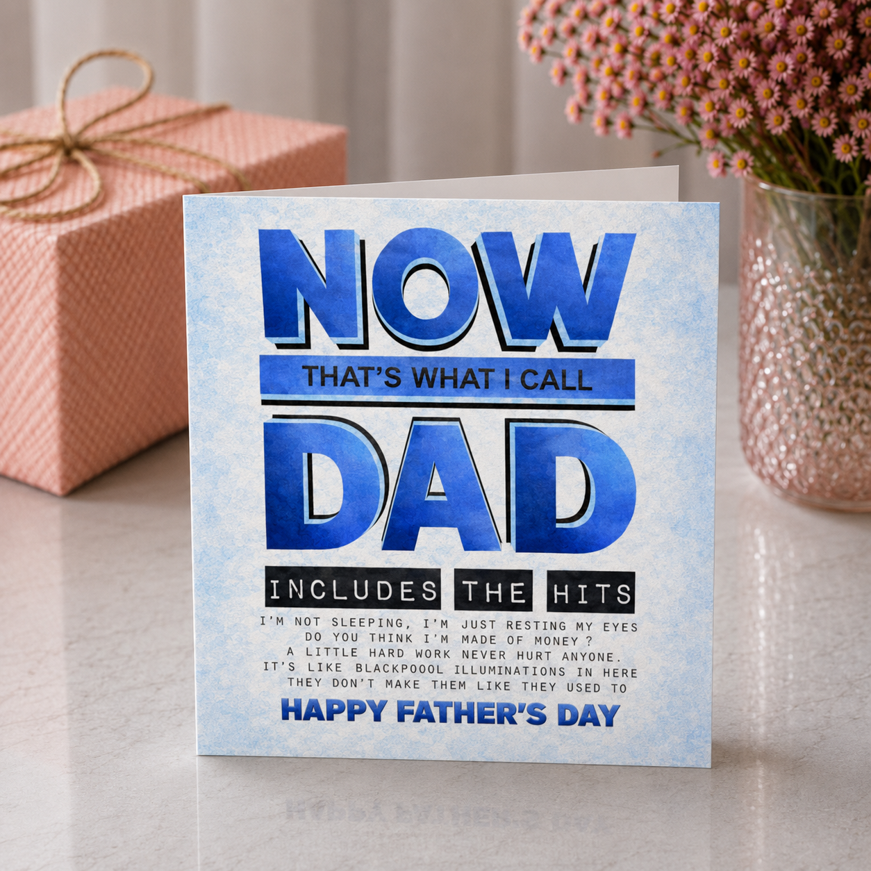 Father's Day card with blue text on a light background, gift box, and vase in the background.