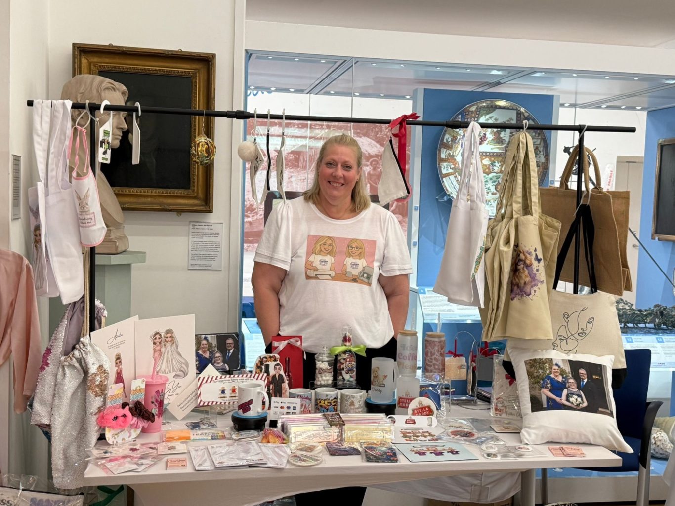 A woman stands proudly behind a display of handmade crafts and merchandise for sale.
