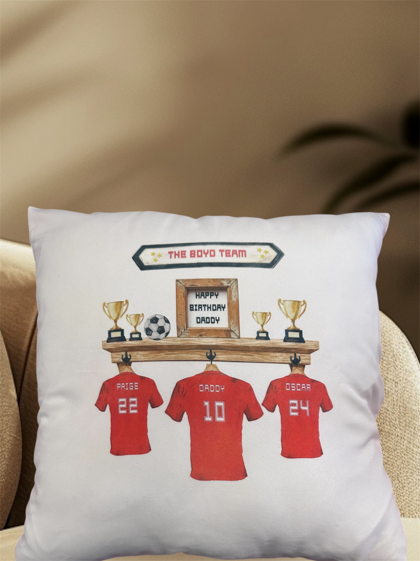 Cushion featuring three red football shirts and trophies on a shelf.